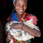 A smiling Ovamwila woman holding her chicken (image by Inger Vandyke)