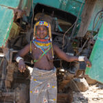 Portrait of an Ovamwila woman with the wreck of an old Russian military truck, a remnant from the Angolan war (image by Inger Vandyke)