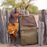 An Ovandimba man standing beside the armoured military vehicle door which is used as the gate to his compound (image by Inger Vandyke)