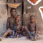 An Ovandimba mother with her children outside their brightly painted home (image by Inger Vandyke)