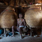 Inside her home an Ovandimba woman sits between two gigantic granary baskets that she has woven (image by Inger Vandyke)