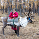 A young Tsaatan girl laughs with her Reindeer (image by Inger Vandyke)