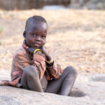 A young Laarim child sitting in a grain grinding pit (image by Inger Vandyke)