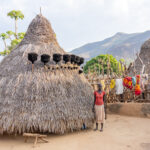 A Lopit woman stands outside her traditional home (image by Inger Vandyke)