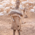 A Mundari boy carries his goat across the camp (image by Inger Vandyke)