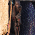 At sunrise, a Mundari girl emerges from her makeshift tent (image by Inger Vandyke)
