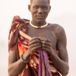 A smiling Mundari man with his 'V' scar and hair dyed orange by cow urine (image by Inger Vandyke)