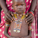 A young Toposa girl in the safe arms of her mother (image by Inger Vandyke)