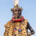 A striking elderlly Toposa woman attends a ceremony wearing a Serval skin, beads and an Ostrich feather (image by Inger Vandyke)