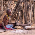 An elderly Toposa woman smoking an Ijoo in front of her home (image by Inger Vandyke)