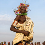 A Toposa woman athletically leaps into the air during a dance, sending her bead decorations flying (image by Inger Vandyke)