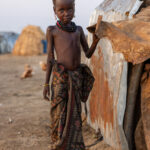 A young Dassanech girl stands in front of her home, which is covered with aluminum sheets (image by Ingrid Koedood)