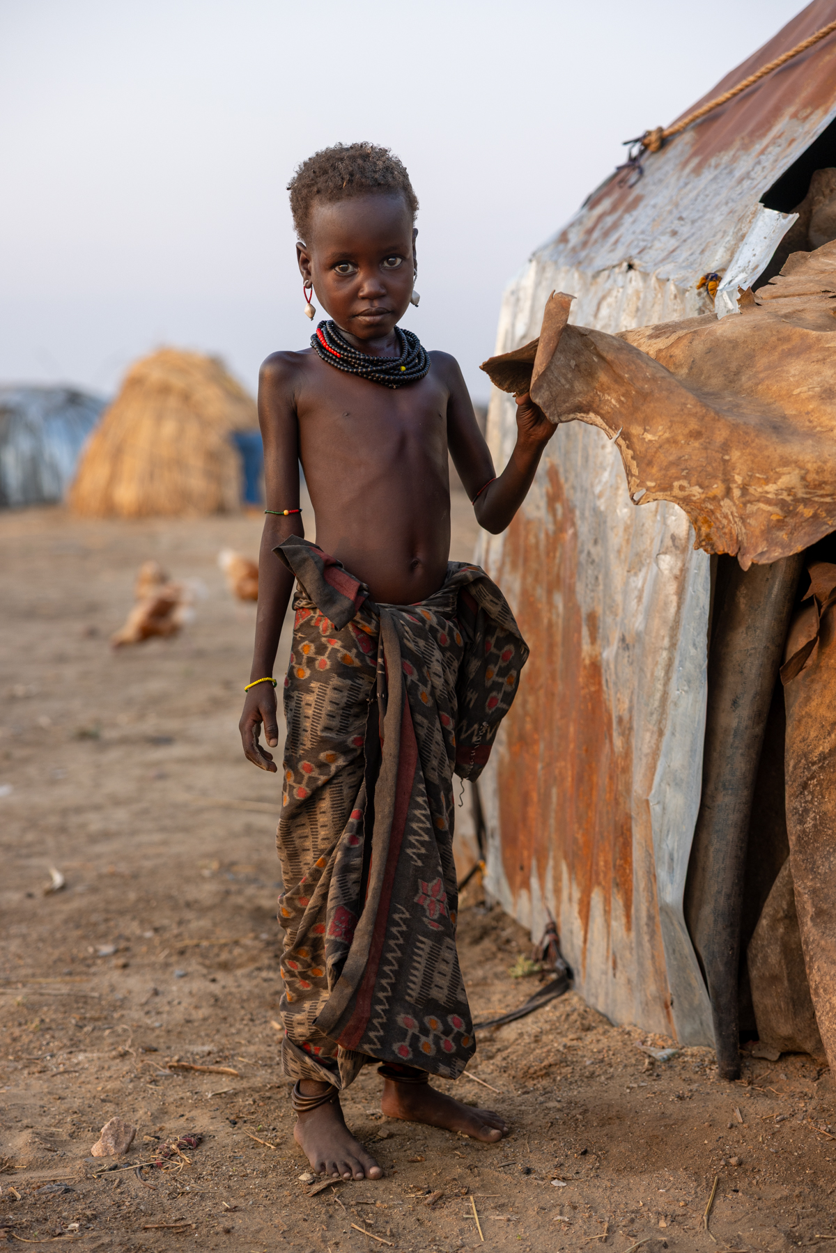 A young Dassanech girl stands in front of her home, which is covered with aluminum sheets (image by Ingrid Koedood)