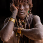 A Hamer woman waits, slightly bored, at the Turmi market as maize is ground into flour (image by Ingrid Koedood)
