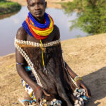 A portrait of a young Karo woman with a painted face, sitting in front of the Omo River (image by Ingrid Koedood)