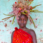 A Suri girl, beautifully adorned with flowers, poses in front of one of the vibrant walls in Kibish town (image by Ingrid Koedood)