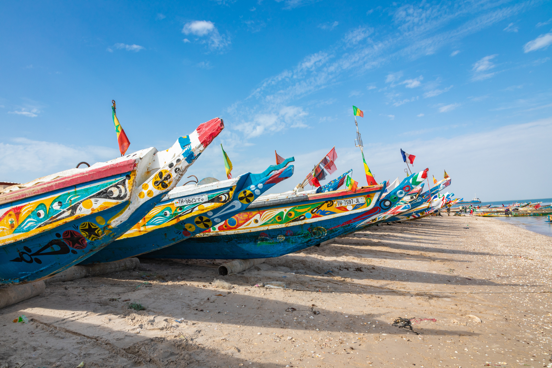 Lines of beautifully painted wooden pirogues line the beach of a fishing village.
