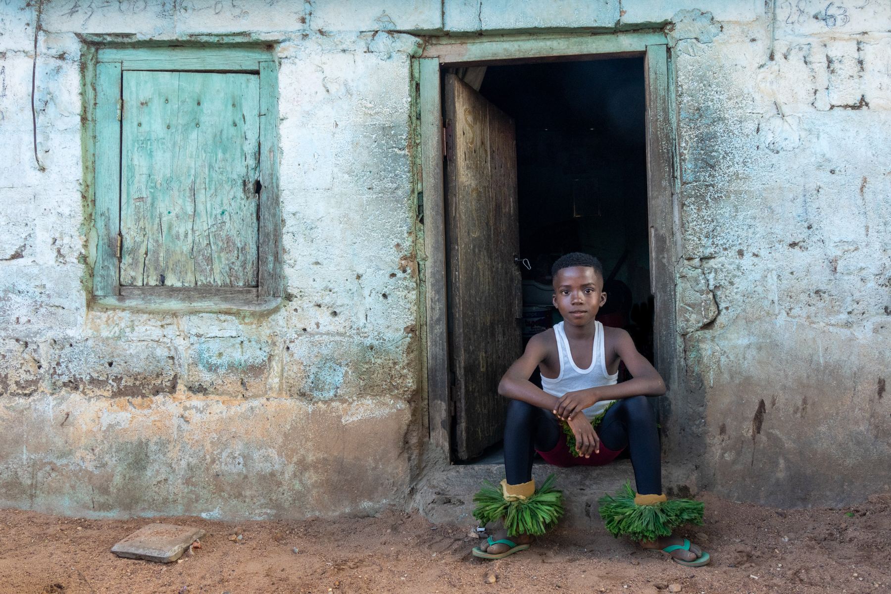 A young Zaouli dancer in the doorway of his home (image by Inger Vandyke)