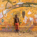 A young boy standing in front of a street art wall in a remote village in Benin (image by Ingrid Koedood)