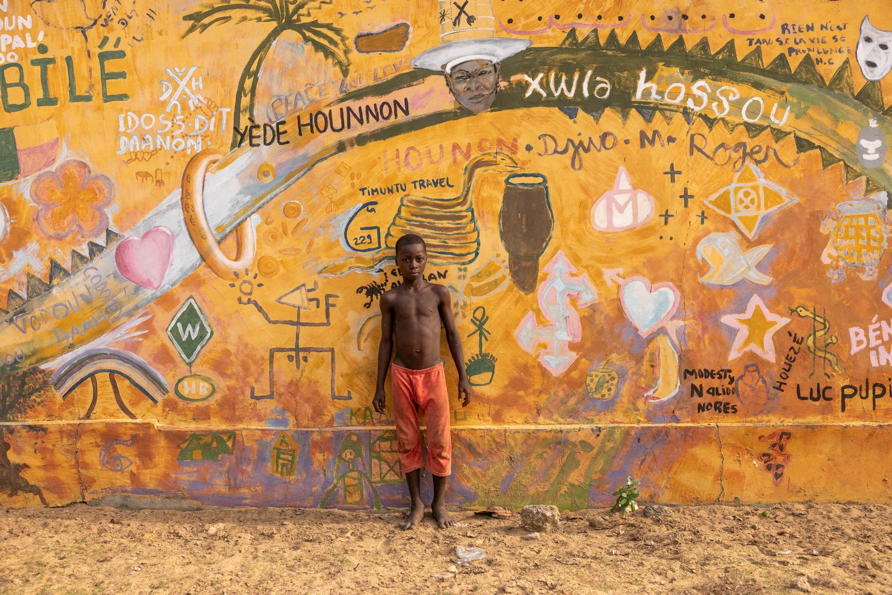 A young boy standing in front of a street art wall in a remote village in Benin (image by Ingrid Koedood)