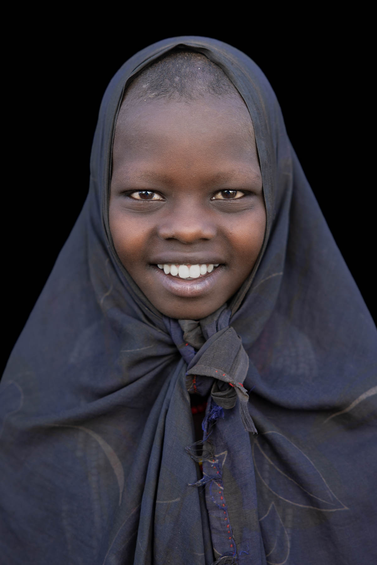 An Arbore girl with a shaved head and a bright smile, colorful beads hidden beneath her scarf. (image by Ingrid Koedood)