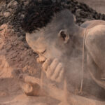 A young Mundari man 'makes up' his face with ash and dust from the fire (image by Inger Vandyke)