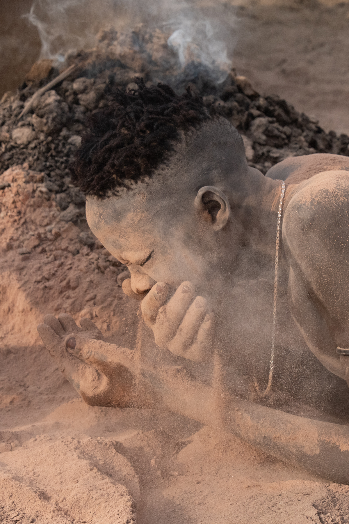 A young Mundari man 'makes up' his face with ash and dust from the fire (image by Inger Vandyke)