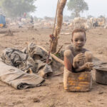 A Mundari boy sitting in a bucket that he would normally use to collect dung (image by Inger Vandyke)