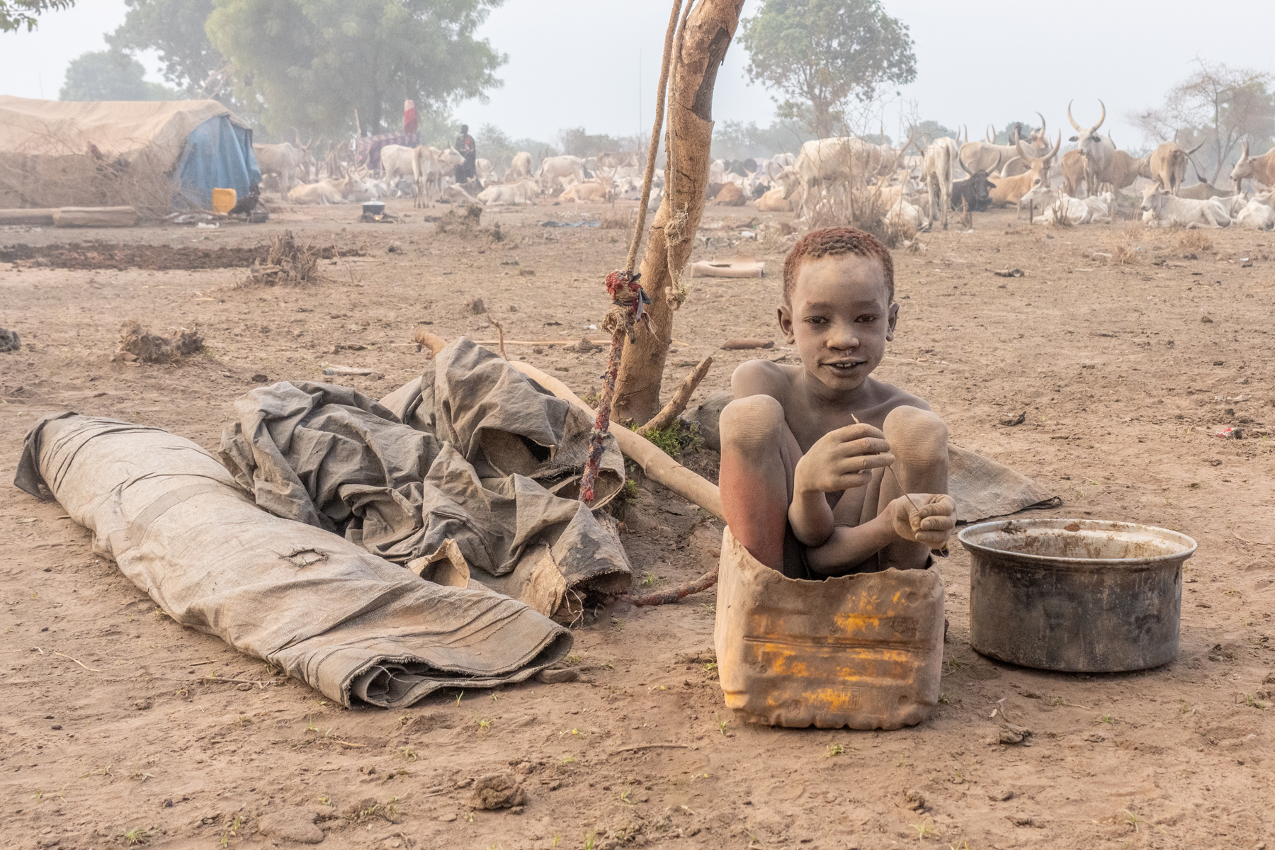 A Mundari boy sitting in a bucket that he would normally use to collect dung (image by Inger Vandyke)