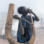 A young Mundari man playing music on a ceremonial Tung horn (image by Inger Vandyke)