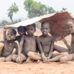 Mundari children take shelter under a cow skin from a light rain shower (image by Inger Vandyke)