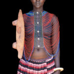Beautiful Mundari woman wearing her bone bracelet, beaded collar and carring a hand-carved wooden seat (image by Inger Vandyke)