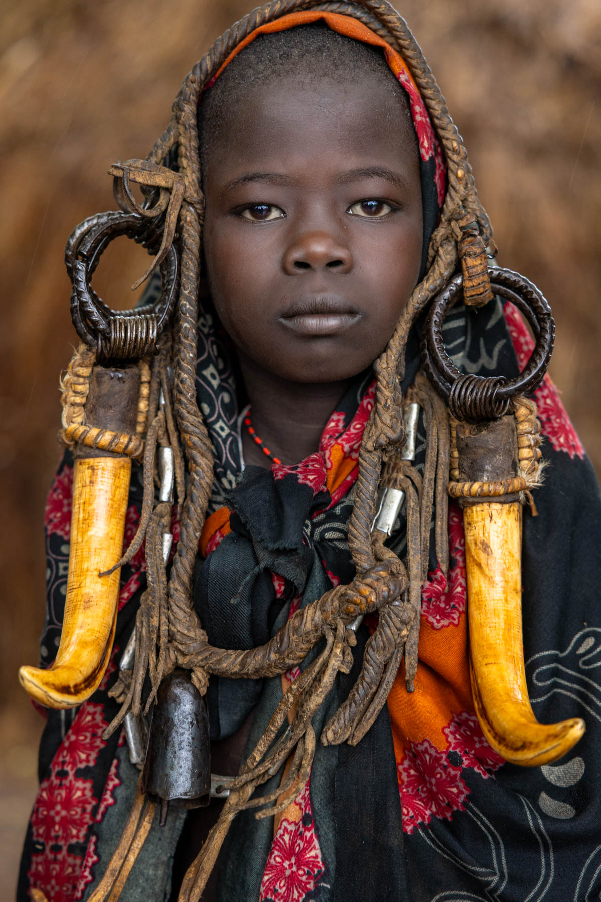 A Mursi girl framed by rich earth tones and vibrant red, her adornments glowing in the warm light. (image by Ingrid Koedood)