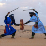 Aroukas warriors engage in a mock sword battle at sunset in the desert (image by Inger Vandyke)