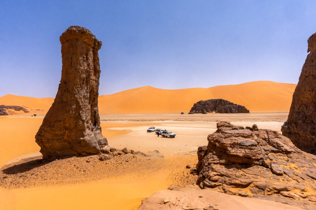 Our expedition vehicles at a stunning clay pan with rock pillars in Tadrart Rouge (image by Inger Vandyke)