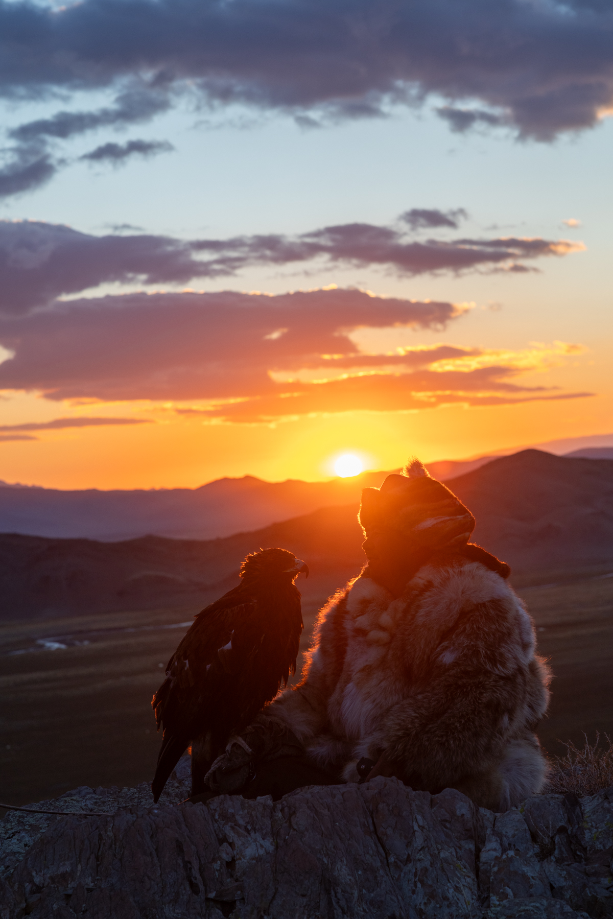 After a cold night in the mountains, the first rays of the rising sun bring warmth to the eagle hunter and his golden eagle (image by Ingrid Koedood)