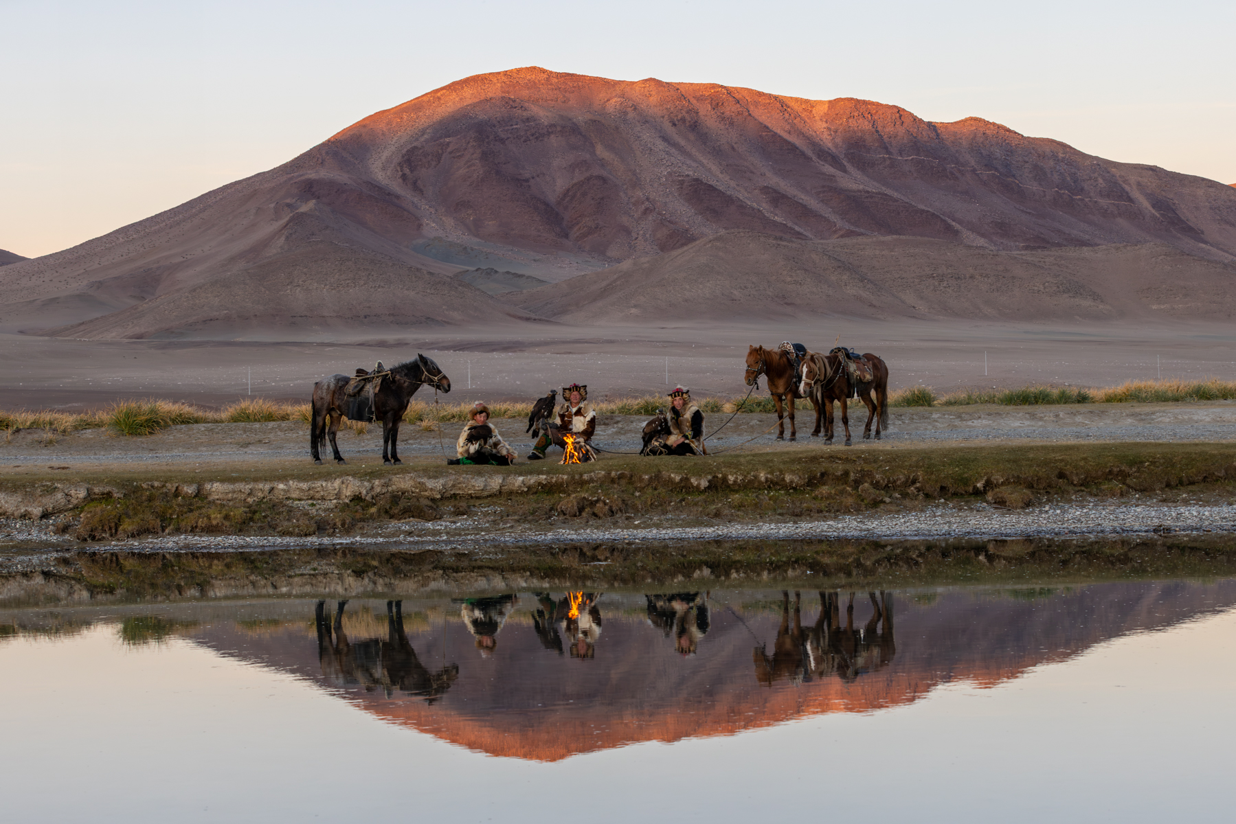 Eagle hunters gathered around the fire, with the mountains and their reflections catching the warm golden light (image by Ingrid Koedood)