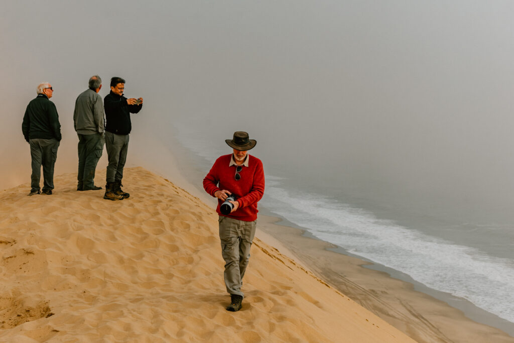 Our Namibia tour-members wait for the famous fog to clear from one of Sandwich Harbour's classic viewpoints. In the end, it didn't clear. But the sight of the Atlantic crashing into great sand dunes was beautiful regardless (image by Virginia Wilde)